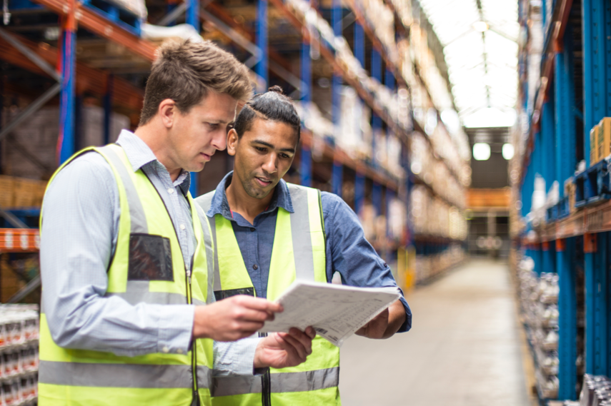 Two workers in a warehouse looking at some paper and discussing..