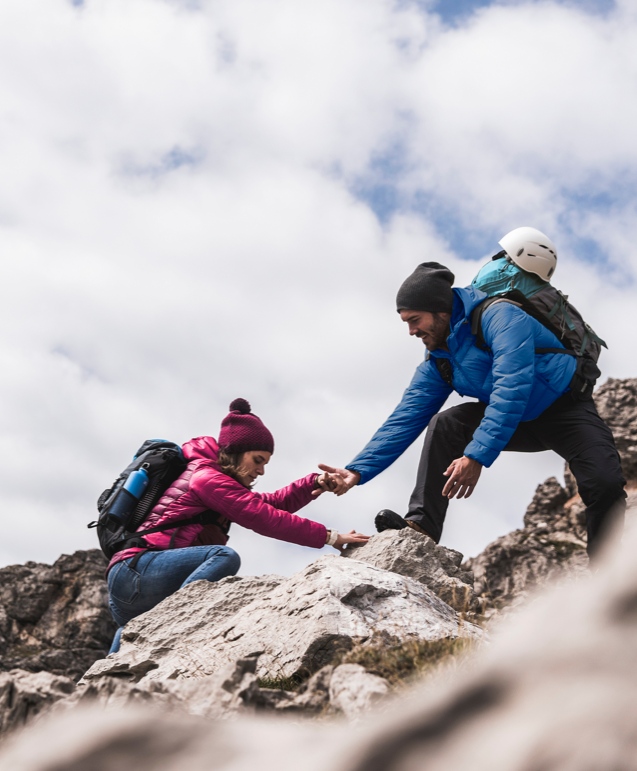 A man helping a woman on hike to a rocky mountain.